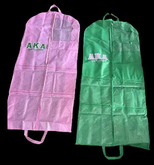 Two zippered garment bags laid flat on a carpeted floor: one pink and one green, each with a large front pocket and the letters 'AKA' printed on the upper section.